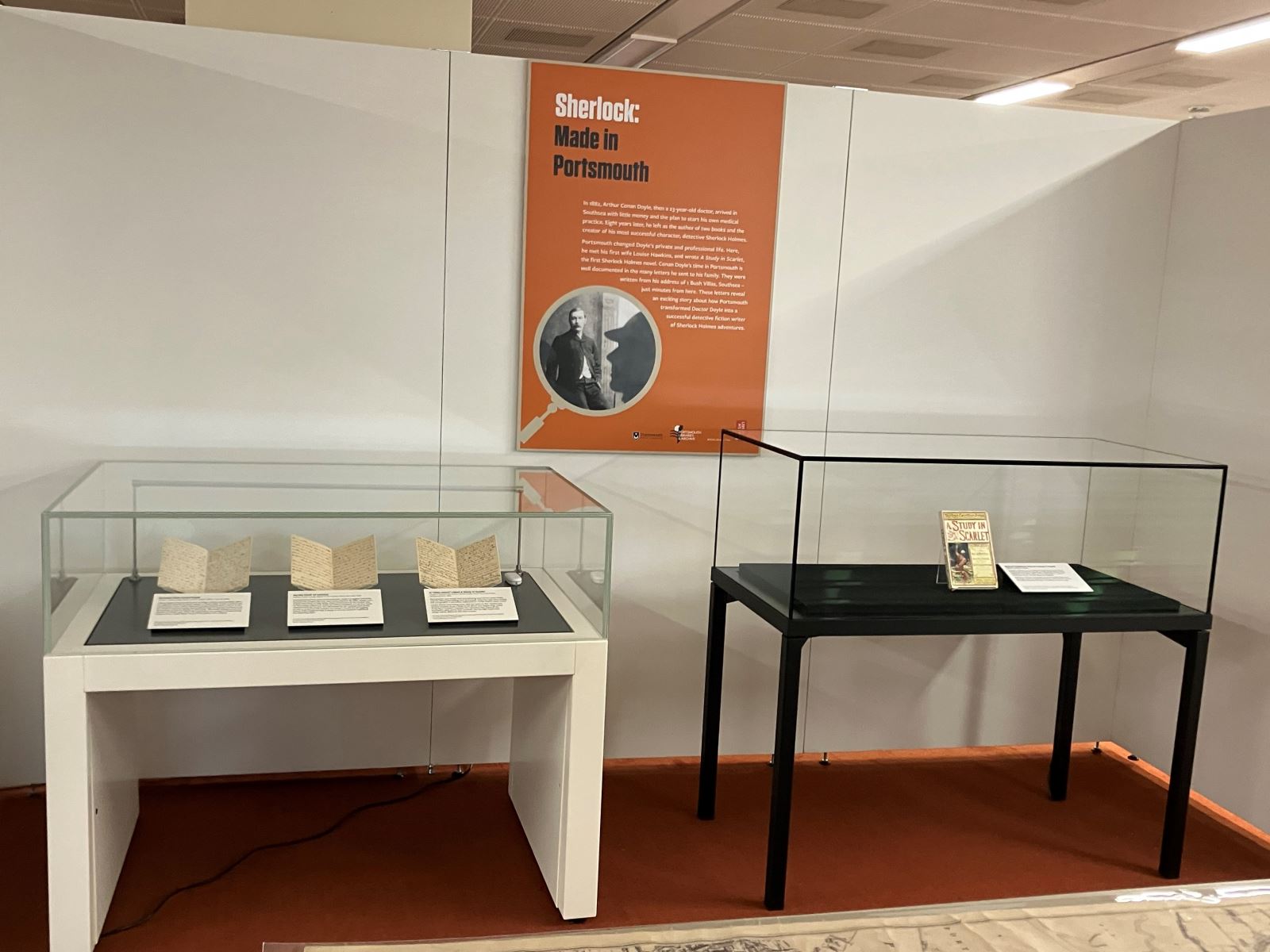 Two display cases, One containing letters written by Conan Doyle, the other containing Beeton's Christmas Annual A Study In Scarlet. Behind them is an info placard titled Sherlock: Made in Portsmouth.